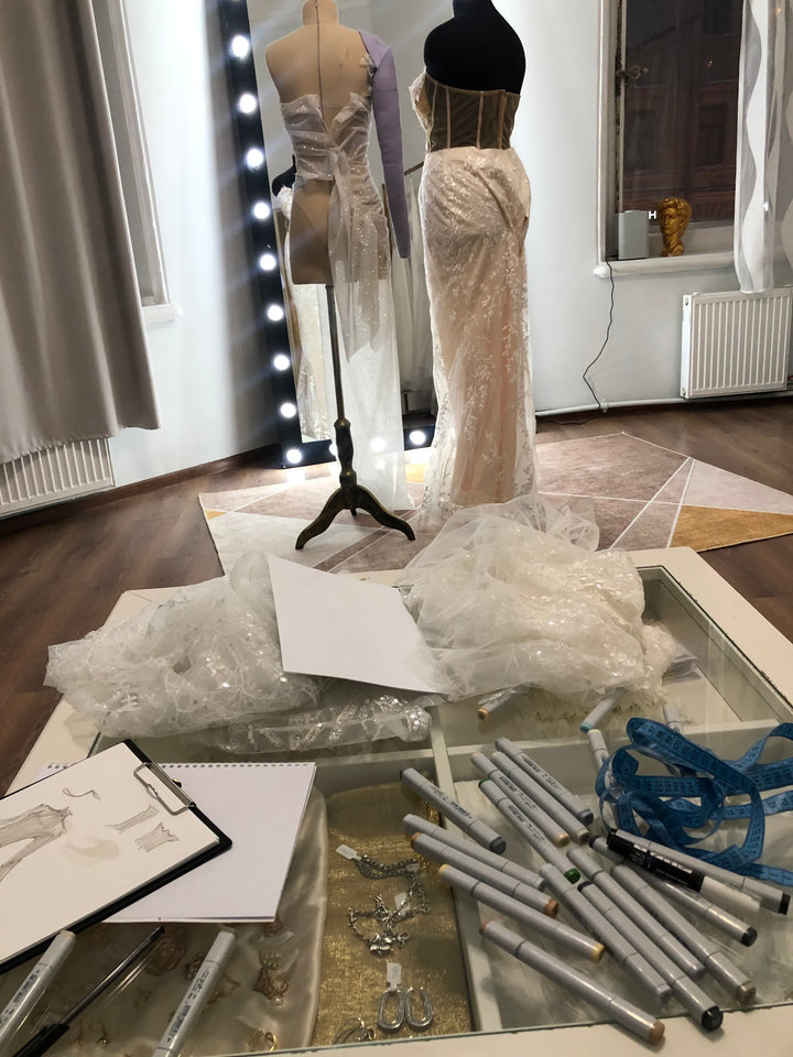 Atelier designer workspace with Copic markers, tape measure, dress sketches and dress forms with gowns in progress